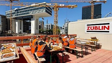 Kinder in Arbeitsschutzkleidung auf einer Baustelle beim Mittagessen