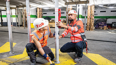 Two workers on the building site are measuring something