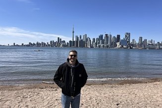 Junger Mann steht am Flussufer, im Hintergrund die Skyline von Toronto