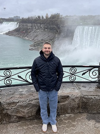 A young man smiles at the camera; Niagara Falls can be seen in the background