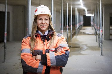 Bild einer jungen Bauleiterin in Arbeitskleidung, die in die Kamera lächelt