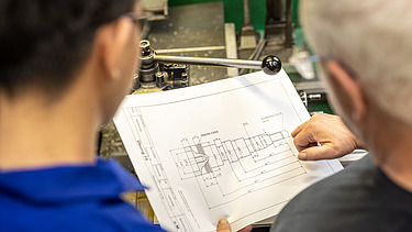 An apprentice and a trainer are looking at a plan