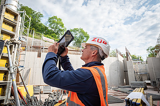 A man in high-visibility workwear on a building site, holding a tablet
