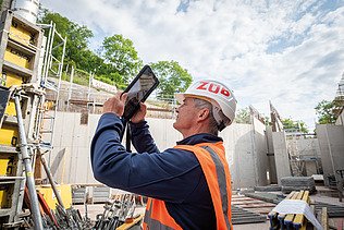 A man in high-visibility workwear on a building site, holding a tablet