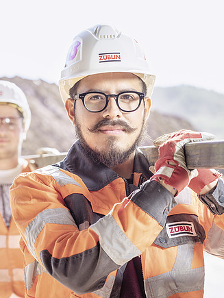 Two men are carrying a steel bar whilst wearing PPE.