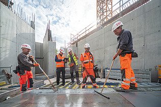 Fünf Personen in Arbeitsschutzkleidung auf der Baustelle am arbeiten