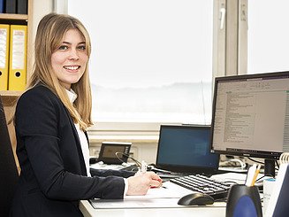Junge Frau an einem Büroarbeitsplatz, lächelt in die Kamera
