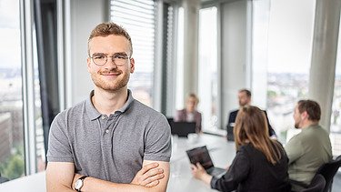 Besprechungssituation, ein Mitarbeiter im Vordergrund mit verschränkten Armen