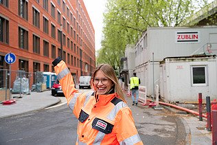 Junge ZÜBLIN Mitarbeiterin mit PSA vor einer Baustelle.