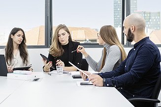 Foto von vier Personen, die mit Tablets am Tisch sitzen und sich anschauen 