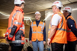 Vier Mitarbeiter in Arbeitsschutzkleidung auf einer Baustelle in einer Besprechungssituation