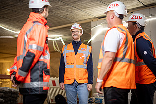 Four employees wearing high-visibility clothing at a building site, in the middle of a meeting