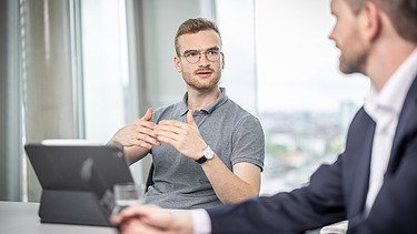 Zwei Mitarbeiter in einer Besprechung, einer mit Tablet gestikuliert