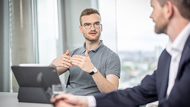 Two staff members in a meeting, one gesticulating with a tablet