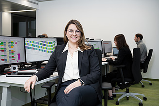 A woman is sitting in front of several screens and smiling at the camera