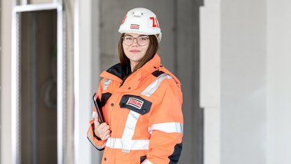 A young woman in high-visibility clothing, smiling at the camera with her arms crossed.