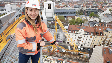Photo of a female site manager standing on a construction crane and pointing towards the building site