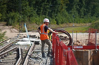 Bauleiter Dominik steht an einem Gerüst und schaut auf eine Baustelle hinunter