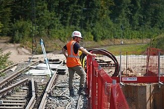 Bauleiter Dominik steht an einem Gerüst und schaut auf eine Baustelle hinunter