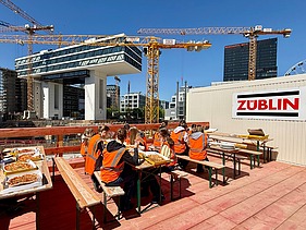 Kinder in Arbeitsschutzkleidung auf einer Baustelle beim Mittagessen