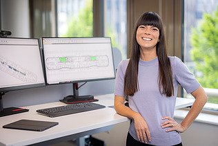 Foto einer ZÜBLIN-Architektin, die an ihrem Büroplatz mit Monitoren in die Kamera lächelt.