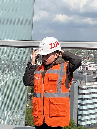 Kind in Arbeitsschutzausrüstung mit ZÜBLIN Helm steht auf Baustelle.