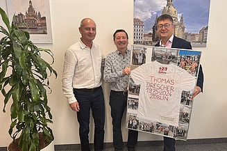 Three colleagues in the office; one of them is holding a picture frame containing a collage