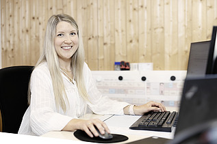 Foto von einer Frau, die im Büro vor dem Bildschirm sitzt und lächelt