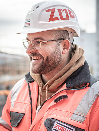 ZÜBLIN Mitarbeiter mit Bauhelm lächelt neben die Kamera.
