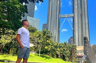 Junger Mann in einem Park, im Hintergrund ist ein Hochhaus zu sehen.