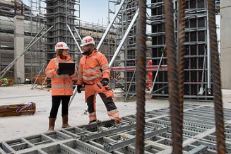 Zwei Mitarbeitende in Arbeitsschutzkleidung auf einer Großbaustelle.
