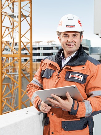 Mitarbeiter steht mit Tablet in der Hand auf einer Baustelle.