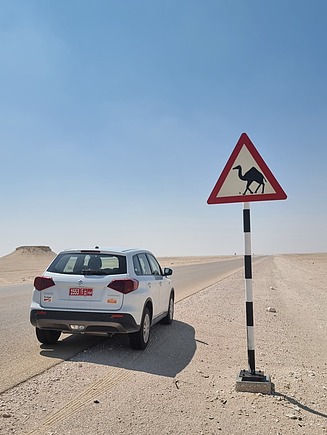 Ein Auto steht in der Wüste, rechts ein Schild 