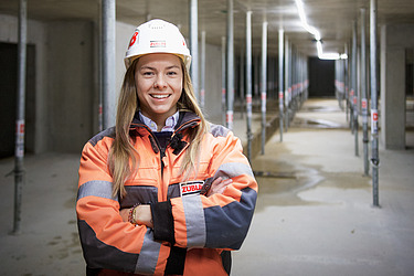 A photo of a young female site manager in her work clothes, smiling at the camera